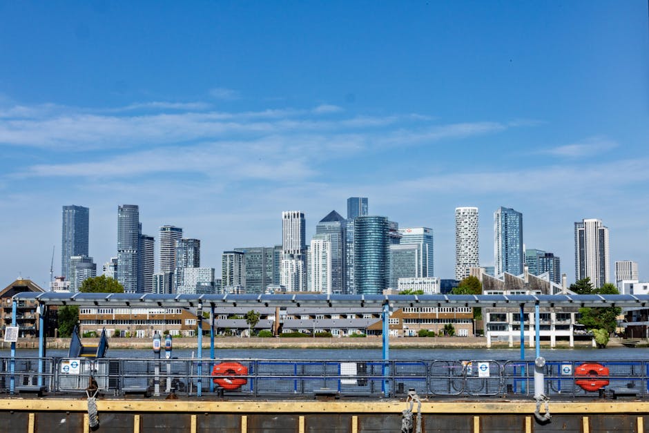 An aerial view of a modern city skyline under a partly cloudy sky, featuring numerous high-rise office buildings and apartments constructed with glass and steel, reflecting light from the clouded sky.